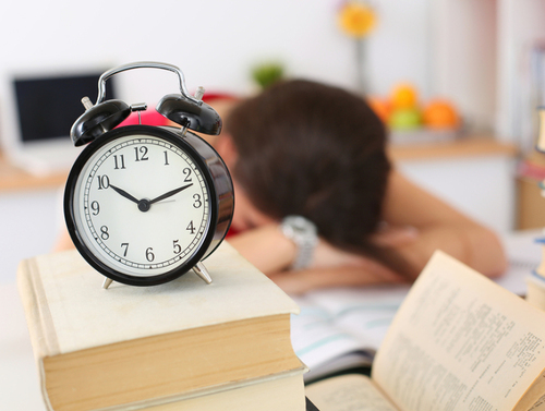 Tired female student at workplace in room taking nap on pile of textbooks. Sleepy brunette woman resting during education after sleepless night. Student in despair caused by exam deadline concept